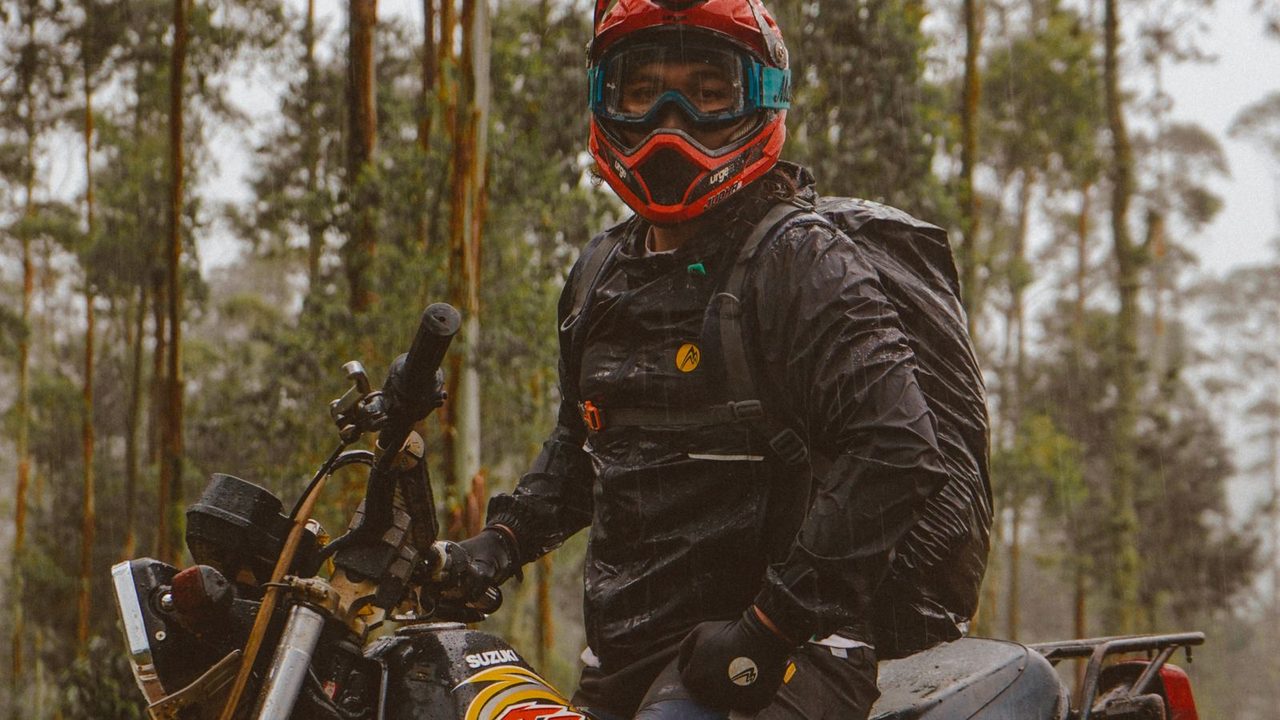 Motorista con casco y gafas junto a su moto en el bosque