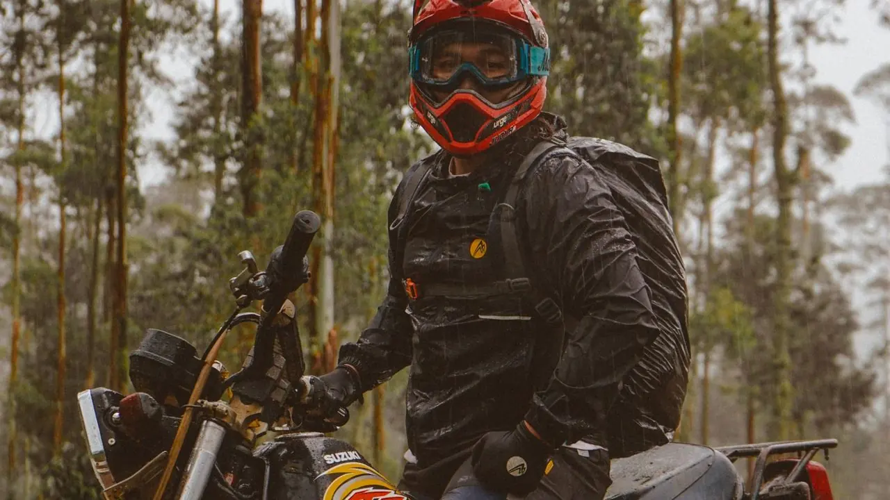 Motorista con casco y gafas junto a su moto en el bosque