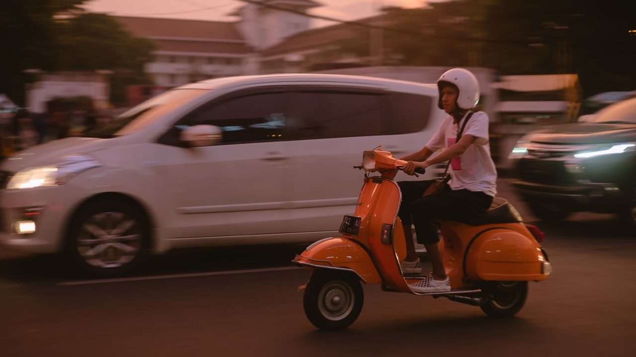 Motorista con casco jet en una Vespa naranja por la ciudad