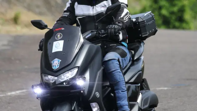 Motorista con casco y equipación en un scooter por la carretera